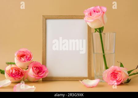 Holzrahmen mit leerem, weißem Papier und zarten Rosen auf beigefarbenem Hintergrund. Minimale trendige Komposition. Romantik Stockfoto