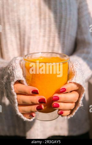 Eine unbekannte Frau, die Kürbis-Smoothie-Latte in der Hand hat. Herbstkaffee mit würzigem Kürbisgeschmack, heißes Getränk der Saison. Herbst-Dri Stockfoto