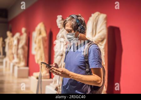 Porträt eines zeitgenössischen Mannes, der sich Skulpturen ansieht und Audioguide auf der Museumsausstellung hört Stockfoto