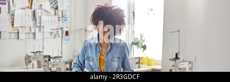 In der modernen Werkstatt zeichnet eine stilvolle afroamerikanische Dame mit Schneiderkreide Muster auf Stoff Stockfoto