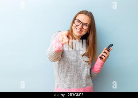 Eine Frau mit Brille, die ihr Smartphone hält und mit dem Zeigefinger auf die Kamera zeigt Stockfoto