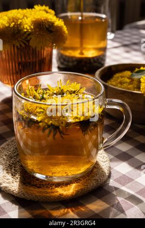 Löwenzahnblume gesunder Tee in Glas Teekanne und Glasbecher auf dem Tisch. Köstlicher heißer Kräutertee aus frischen Löwenzahn-Blumen bei Ho Stockfoto