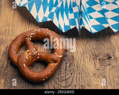 Leckere Brezel mit bayerischer Flagge auf einem rustikalen Holztisch, Oktoberfest oder traditionelles bayerisches Speisekonzept Stockfoto