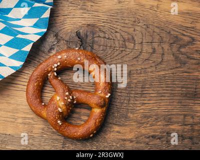 Leckere Brezel mit bayerischer Flagge auf einem rustikalen Holztisch, Oktoberfest oder traditionelles bayerisches Speisekonzept Stockfoto