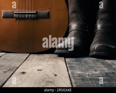 Alte Cowboystiefel mit einer akustischen Gitarre auf Scheunenholz, Platz für Ihren Text Stockfoto