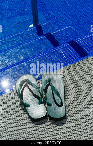 Grüne Flip-Flops auf den Eingangsstufen eines blauen Swimmingpools Stockfoto