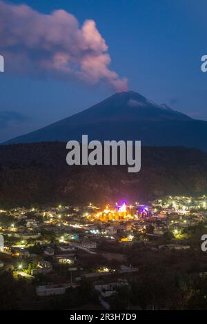 Santiago Xalitxintla, Mexiko. 23. Mai 2023. Die Lichter der Stadt leuchten, während der Vulkan Popocatepetl Asche, Dampf und Gas im Hintergrund aussendet. Popocatépetl ist einer der aktivsten Vulkane in Mexiko. Es gibt seit Tagen Asche, Dampf und Gas aus. Die Experten gingen jedoch davon aus, dass die vulkanische Aktivität begrenzt sein wird, wie von der Behörde für Katastrophenschutz berichtet wurde. Kredit: Celacanto//dpa/Alamy Live News Stockfoto