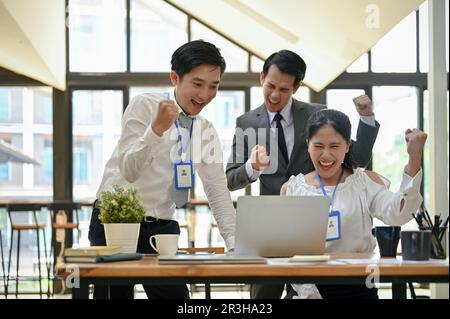 Eine Gruppe von überfreulichen und fröhlichen asiatischen Geschäftsleuten zeigt ihre Fäuste, freut sich und feiert den Erfolg ihres Projekts. Stockfoto