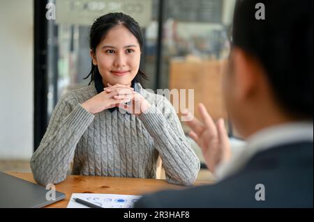 Eine attraktive und inspirierte junge asiatische Büroangestellte konzentriert sich darauf, ihrem Chef zuzuhören, der sie über ein Projekt im Büro informiert. Stockfoto
