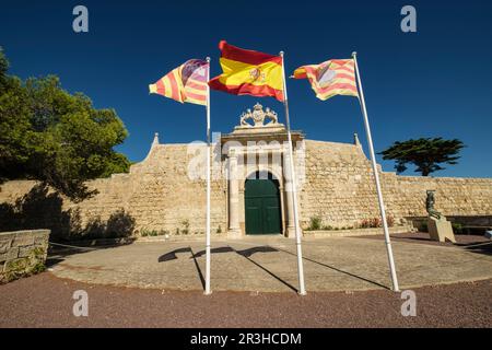 Spanische und balearische Flaggen, Puerta de los Leones, Haupteingang der Insel Lazareto, ehemaliges Militärkrankenhaus, Illa del Llatzeret, Innere des Hafens von Mahon, Menorca, balearen, Spanien. Stockfoto