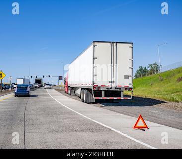 Gebrochener roter großer Sattelschlepper in Industriequalität mit offener Motorhaube und trockenem Auflieger, der am Autobahneingang außer Betrieb ist Stockfoto