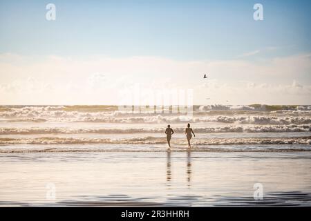 Glückliches Paar läuft in den Wellen im Nordwesten des kalten Pazifischen Ozeans zu schwimmen in Sonnenstrahlen löslich in Sprühnebel atmen gesunde frische Luft Stockfoto