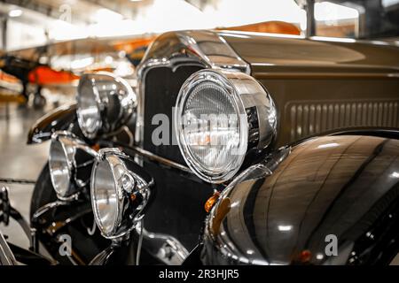 Fragment eines klassischen schwarzen Autos mit überraschend elegantem Kühlergrilldesign, aus Chromstreifen und runden Frontscheinwerfern in einem verchromten Gehäuse, BL Stockfoto