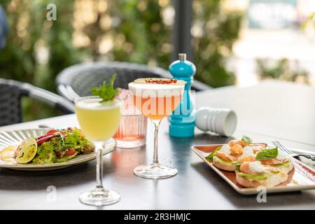 Im Restaurant werden köstliche Bruschettas und Salat mit erfrischenden Cocktails serviert Stockfoto