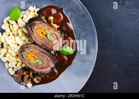 Traditionelle langsam gekochte deutsche Wagyu-Rinderrouladen mit Spaetzle, serviert in scharfer Soße als Draufsicht auf einem Designerteller Stockfoto