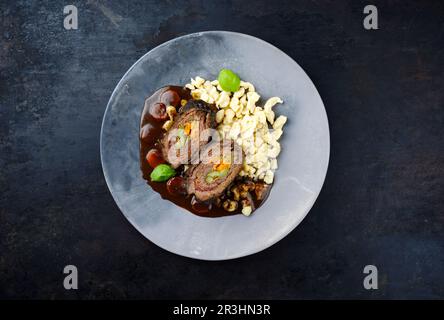 Traditionelle langsam gekochte deutsche Wagyu-Rinderrouladen mit Spaetzle, serviert in scharfer Soße als Draufsicht auf einem Designerteller Stockfoto