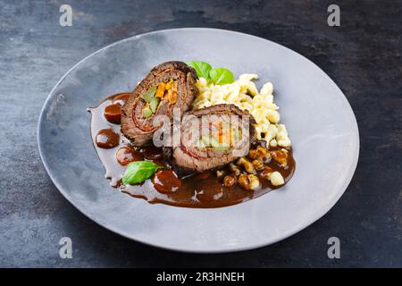 Traditionelle langsam gekochte deutsche Wagyu-Rinderrouladen mit Spaetzle, serviert in scharfer Soße, ganz aus der Nähe auf einer Designerplatte Stockfoto