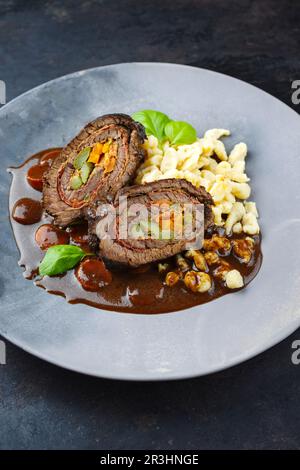 Traditionelle langsam gekochte deutsche Wagyu-Rinderrouladen mit Spaetzle, serviert in scharfer Soße, ganz aus der Nähe auf einer Designerplatte Stockfoto