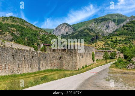 Blick auf die schmale Straße entlang der alten militärisch-alpinen Festung als Berge unter blauem Himmel im Hintergrund in Vinadio, Italien. Stockfoto