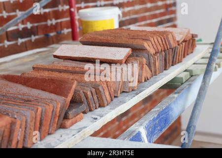 Viele dekorative Ziegel auf Gerüsten im Innenbereich. Installationsvorgang für Fliesen Stockfoto