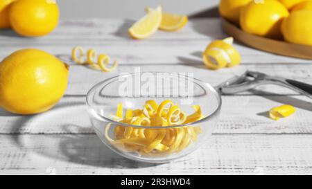 Schüssel mit Schälstücken, frischen Zitronen und Zester auf weißem Holztisch Stockfoto