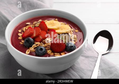 Köstliche Smoothie-Schüssel mit frischen Beeren, Banane und Müsli auf weißem Holztisch, Nahaufnahme Stockfoto