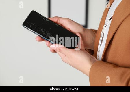 Frau hält ein beschädigtes Smartphone in der Nähe der weißen Wand, Nahaufnahme. Gerät wird repariert Stockfoto