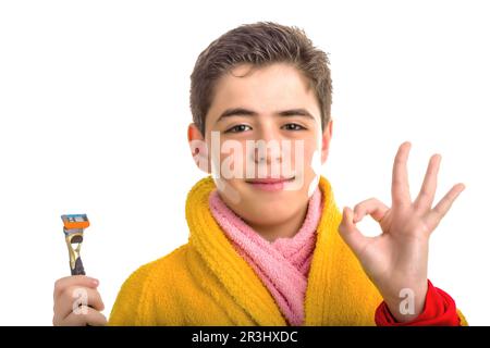 Ein Junge im gelben Bademantel und ein rosafarbenes Handtuch mit einem Rasiermesser macht das OK-Schild Stockfoto