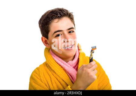 Ein Junge im gelben Bademantel und ein rosa Handtuch lächeln mit dem Rasiermesser, der zum Rasieren verwendet wurde Stockfoto