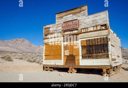 Ein verwittertes, mit Brettern vernageltes Holzgeschäft mit einem Schild „Rhyolite Mercantile“ steht auf einem erhöhten Fundament in der Geisterstadt Rhyolite, Nevada. Stockfoto
