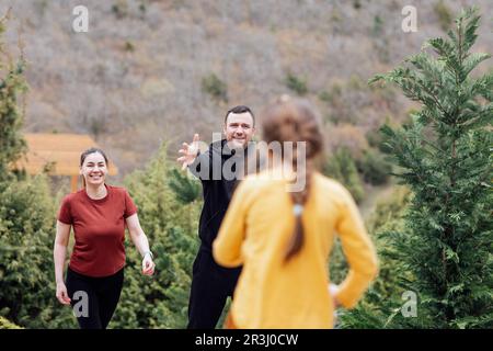Ein kleines Mädchen in gelben Kleidern läuft zu ihren fröhlichen Eltern. Ein lächelndes junges Paar hält seine Hand an seine süße Tochter. Lachender Mann und lachende Frau wi Stockfoto