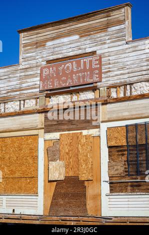 Vertikale Ansicht der falschen Front des Rhyolite Mercantile mit seinem verblassten Schild, verbarrikadiertem Eingang und verwittertem weißem Seitenverkleidungen in der Geisterstadt Rhyolite, Nevada. Stockfoto