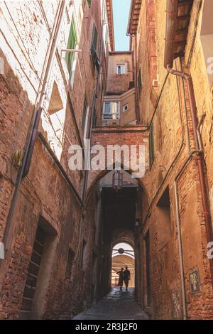 Siena, Italien, 2023. Mai 23: Ein Paar, das in einer engen Straße in Siena spaziert. Vetikal. Silhouette. Speicherplatz kopieren. Stockfoto