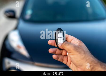 Eine Person, die eine schlüssellose Fernbedienung in der Hand hält, indem sie die Entriegelungstaste drückt. Selektiver Fokus mit unscharfem Hintergrund Stockfoto