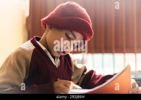 Ein indischer Junge, der im Klassenzimmer lernt, auf einem Notizblock schreibt und seine Schuluniform trägt, Bildung und wieder-zur-Schule-Konzept. Stockfoto