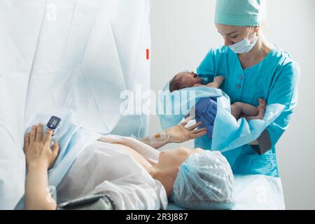 Krankenschwester hält neugeborenes Baby in der Nähe der Mutter im Krankenhaus Stockfoto