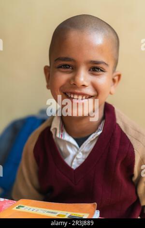 Ein glücklicher Indianerjunge sitzt im Klassenzimmer, trägt seine Schuluniform und lächelt, Bildung und wieder-in-die-Schule-Konzept. Stockfoto