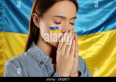 Traurige junge Frau mit gefalteten Händen nahe der ukrainischen Flagge Stockfoto