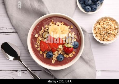 Köstliche Smoothie-Schüssel mit frischen Beeren, Banane und Müsli auf weißem Holztisch, flach liegend Stockfoto