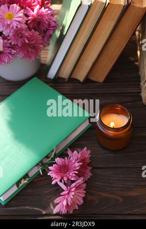 Buchen Sie mit wunderschönen Chrysanthemen als Lesezeichen und Kerze auf einem Holztisch, über dem Blick Stockfoto