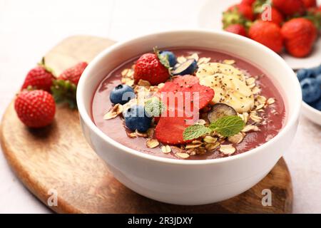 Köstliche Smoothie-Schüssel mit frischen Beeren, Banane und Müsli auf dem Tisch, Nahaufnahme Stockfoto
