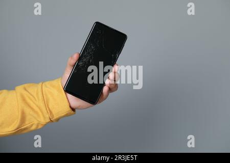 Mann hält ein beschädigtes Smartphone auf hellgrauem Hintergrund, Nahaufnahme mit Platz für Text. Gerät wird repariert Stockfoto