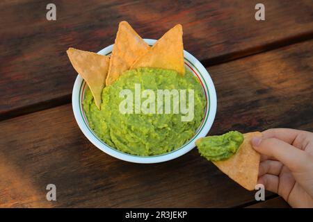 Eine Frau mit Nacho-Chips und köstlicher Guacamole aus Avocados auf einem Holztisch, Nahaufnahme Stockfoto