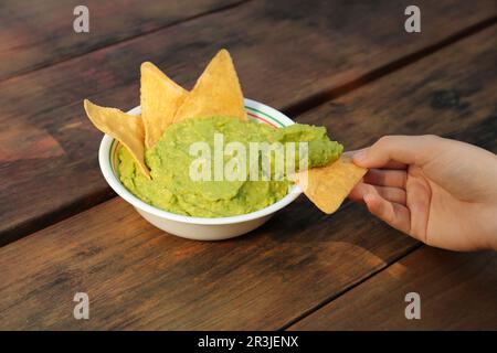 Eine Frau mit Nacho-Chips und köstlicher Guacamole aus Avocados auf einem Holztisch, Nahaufnahme Stockfoto