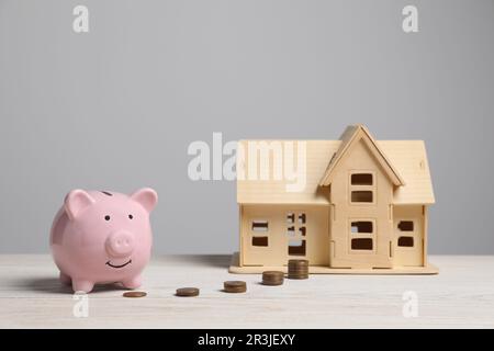 Sparschwein, kleines Hausmodell und Münzen auf einem weißen Holztisch Stockfoto