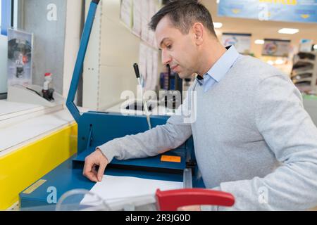 Ein Mann schneidet Papier mit einer großen Papierschneider auf dem Tisch Stockfoto