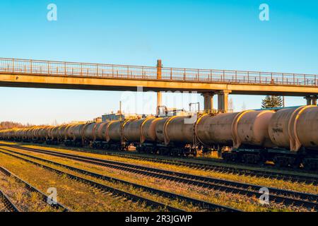 Langer Zug mit Kesselwagen hintereinander in einer Reihe auf einem Gleis neben leeren Schienen Stockfoto