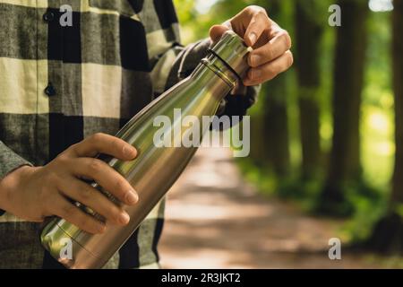 Nahaufnahme einer nicht erkennbaren Wasserflasche mit der Hand. Wiederverwendbare Wärmflasche aus Stahl im Park. Nachhaltiger Lebensstil. Stockfoto