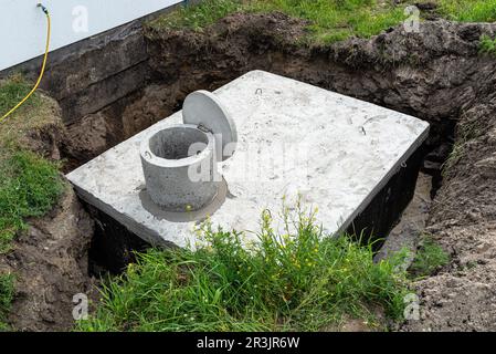 Klärbehälter aus Beton mit einem Fassungsvermögen von 10 Kubikmetern im Garten neben dem Haus, sichtbares Wasser darunter. Stockfoto