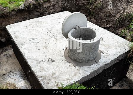 Klärbehälter aus Beton mit einem Fassungsvermögen von 10 Kubikmetern im Garten neben dem Haus, sichtbares Wasser darunter. Stockfoto